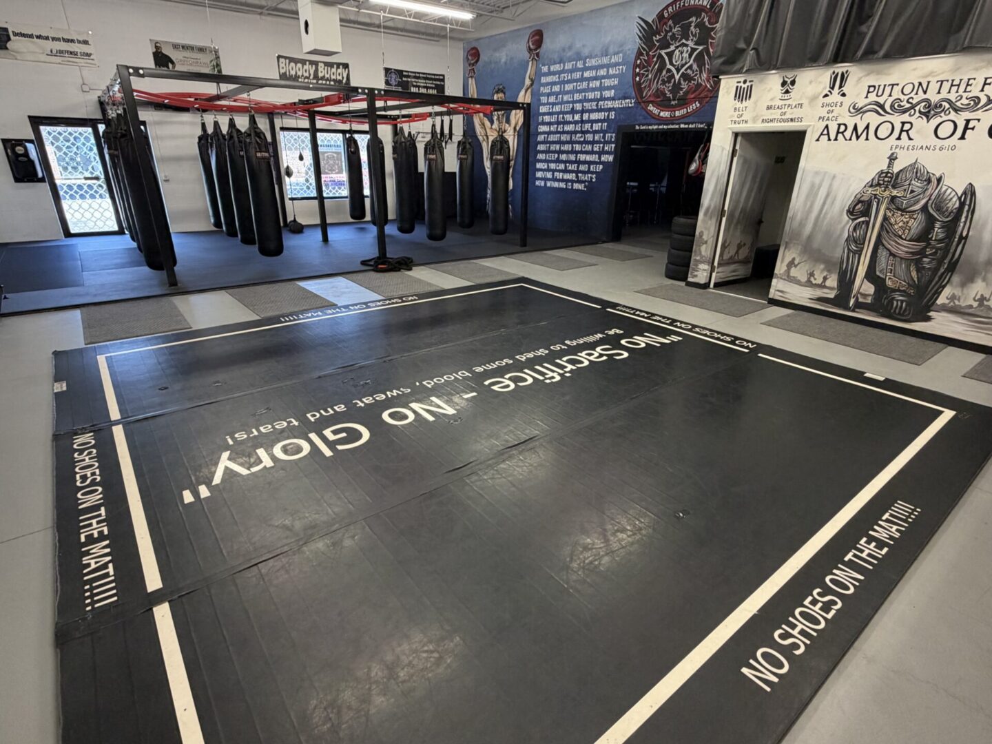 Gym with a black mat on the floor with the words "No Shoes on the Mat" written on it